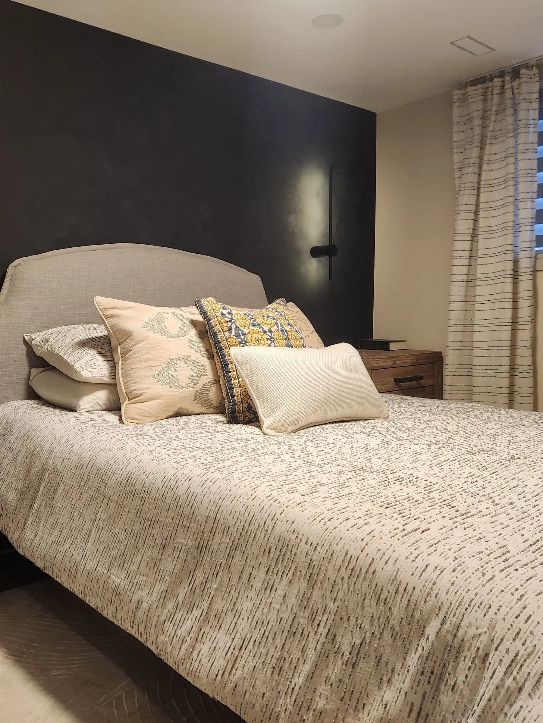A finished basement bedroom with a dark feature wall, wall lights and a wide window